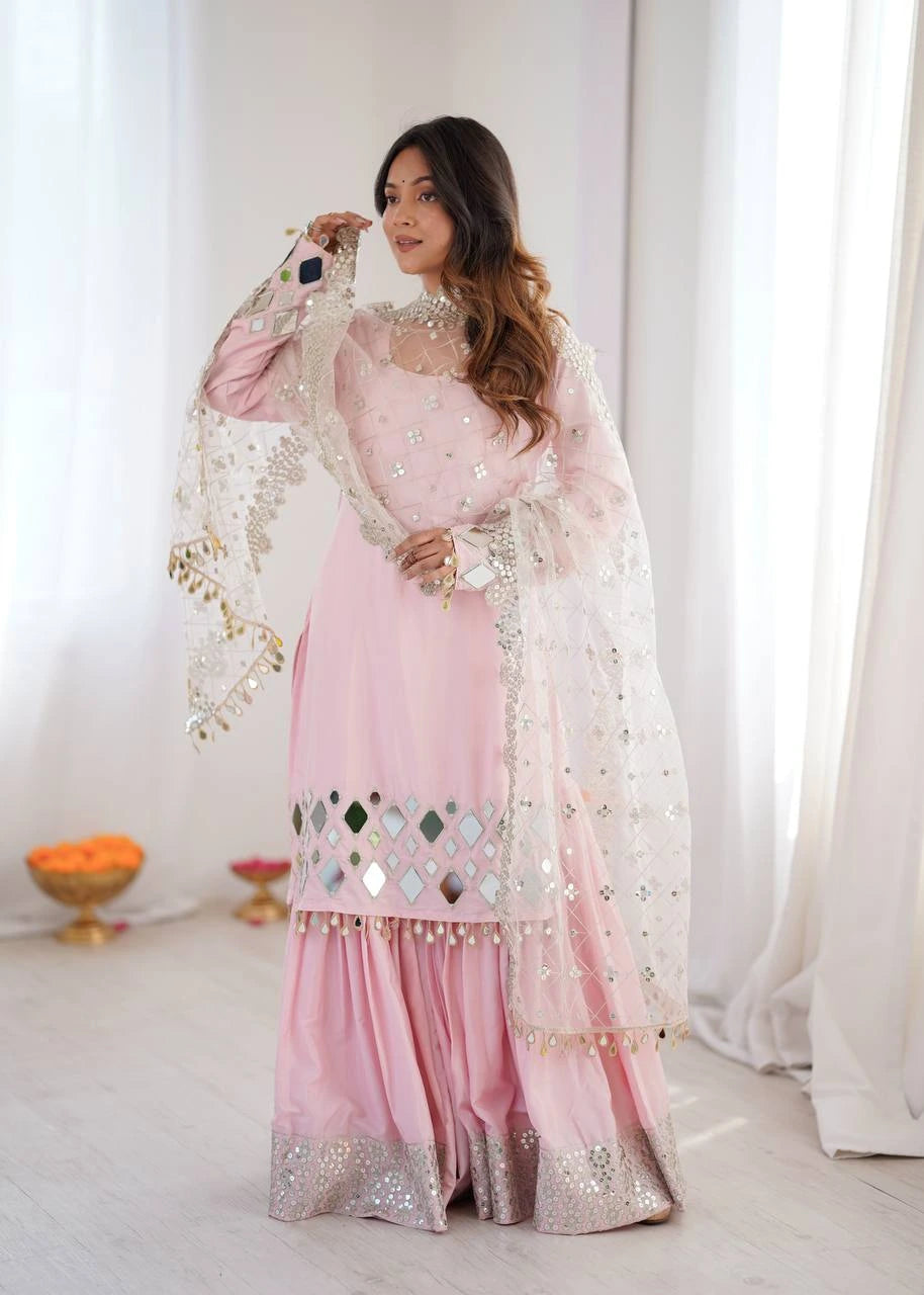 Woman in a pink traditional outfit with a white dupatta against a white curtain background