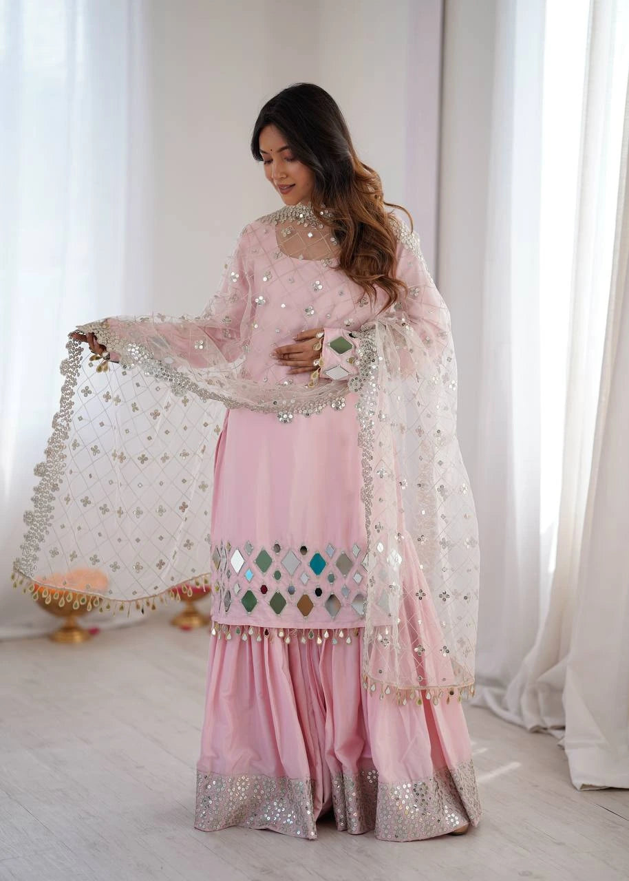 Woman in a pink traditional outfit with a sheer dupatta in a bright room.
