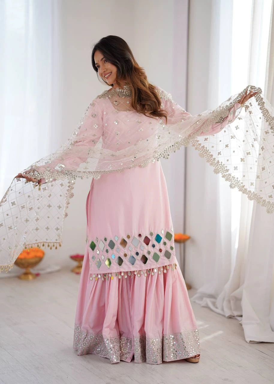 Woman in a pink traditional outfit with intricate designs in a bright room.