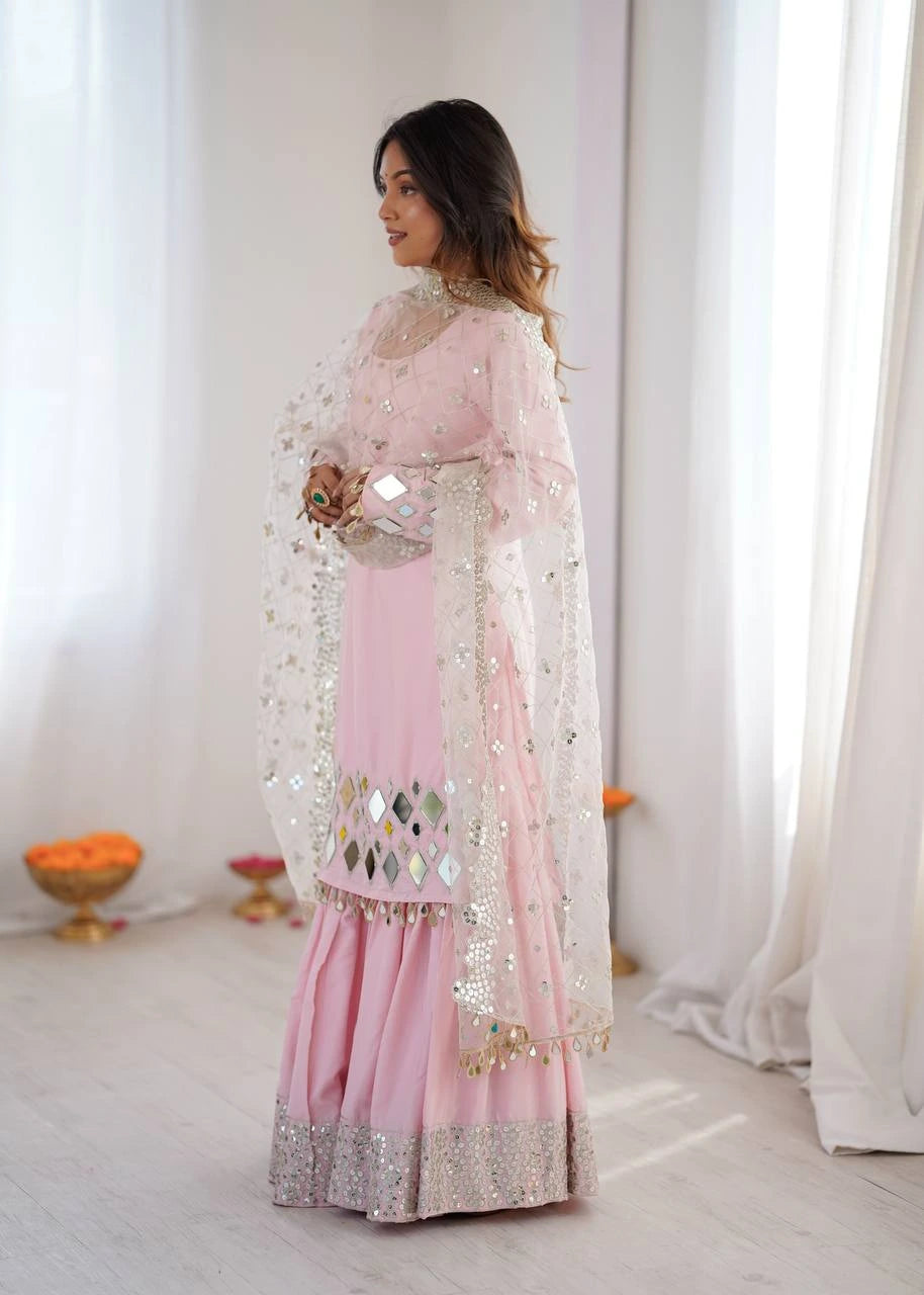Woman in a pink traditional outfit with sequin details standing in a bright room.