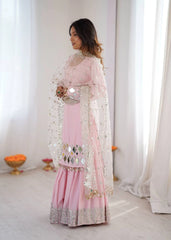 Woman in a pink traditional outfit with sequin details standing in a bright room.