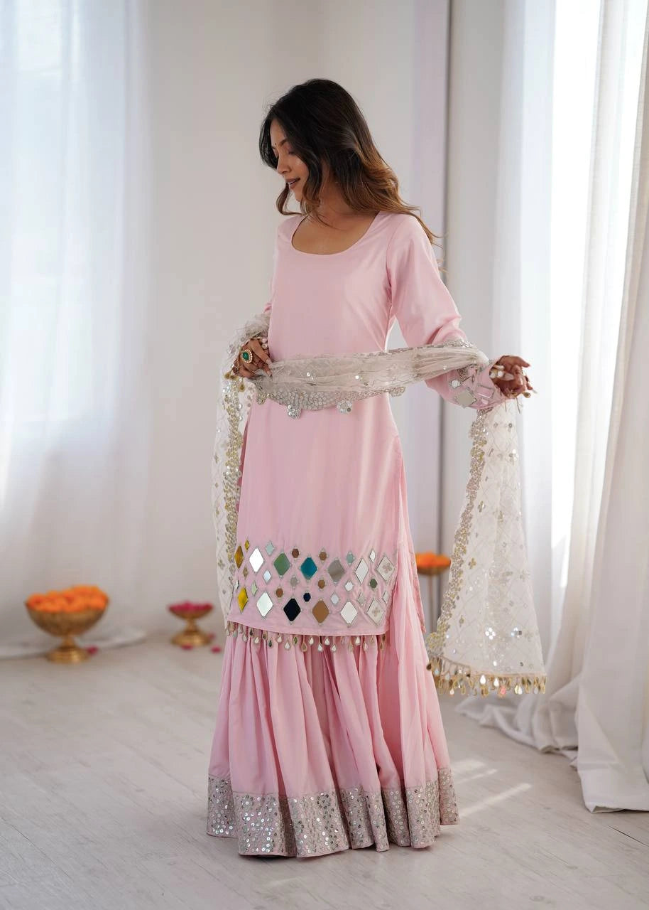 Woman in a pink traditional outfit with decorative shawl in a bright room.