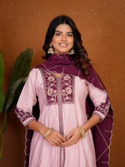 Woman wearing a pink traditional outfit with purple embroidery against a brown background