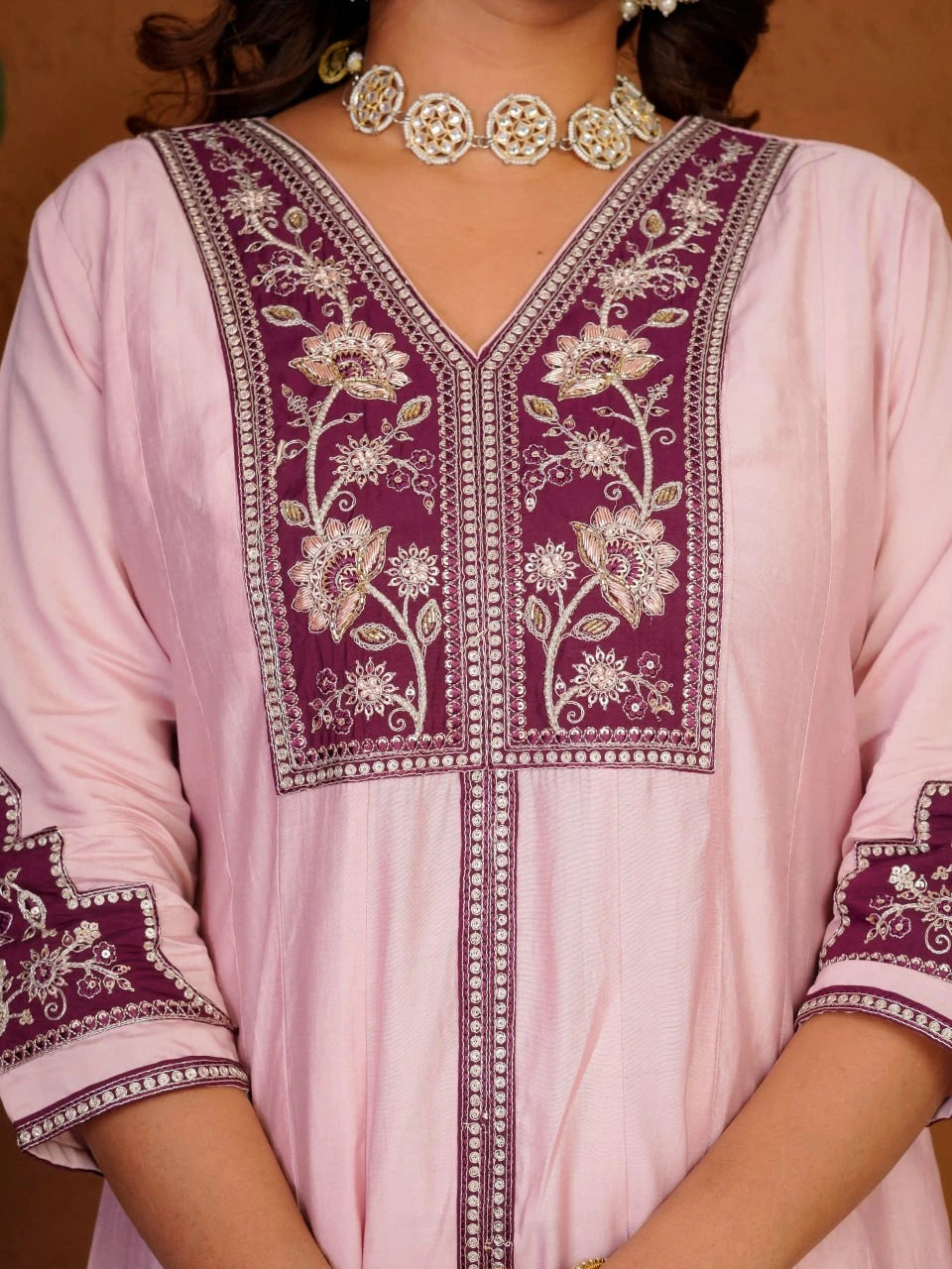 Pink traditional outfit with intricate purple embroidery and a matching necklace.
