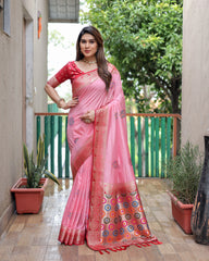 Woman wearing a pink saree with a decorative border on a balcony.