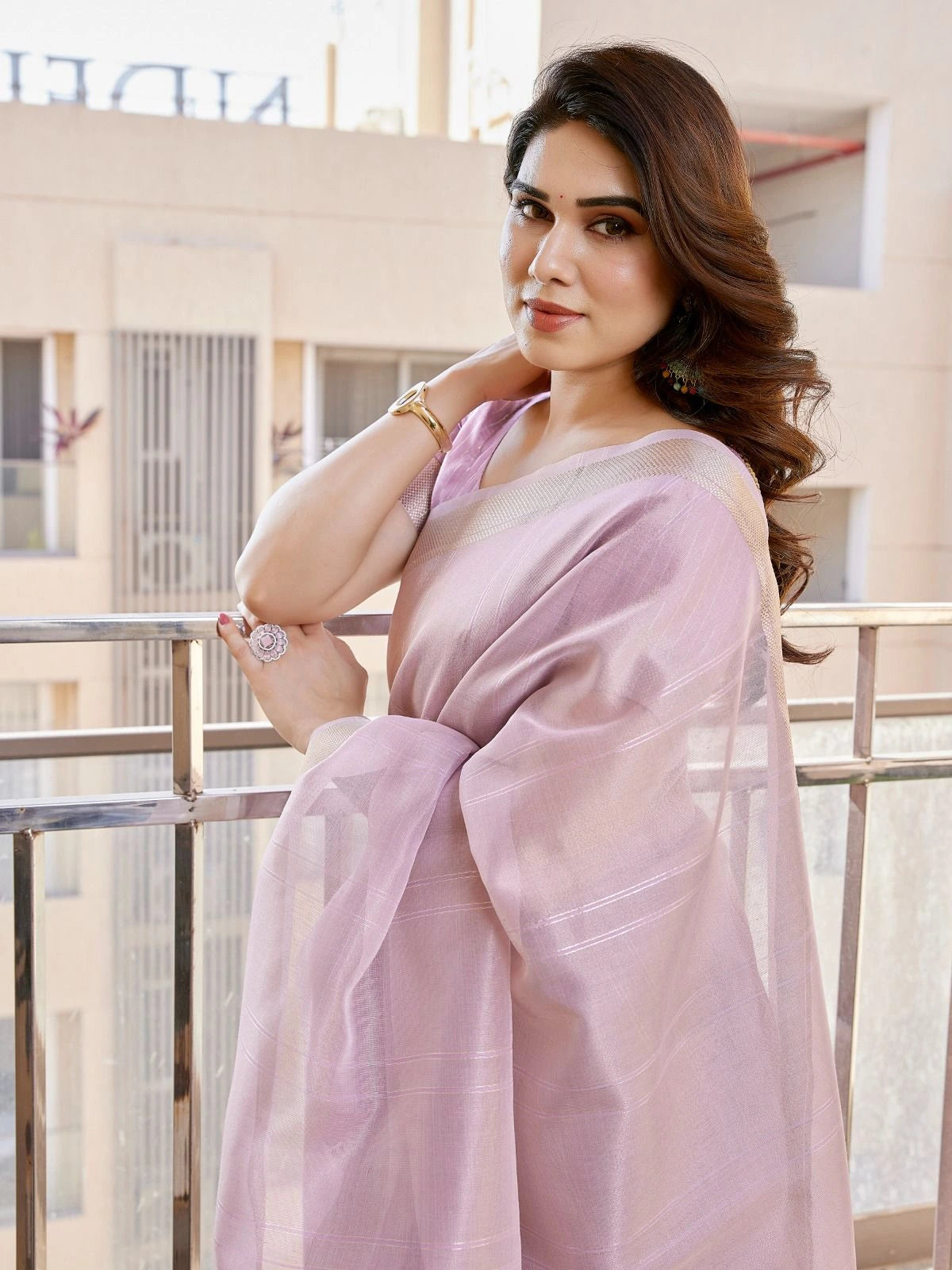 Woman in a light pink saree standing on a balcony