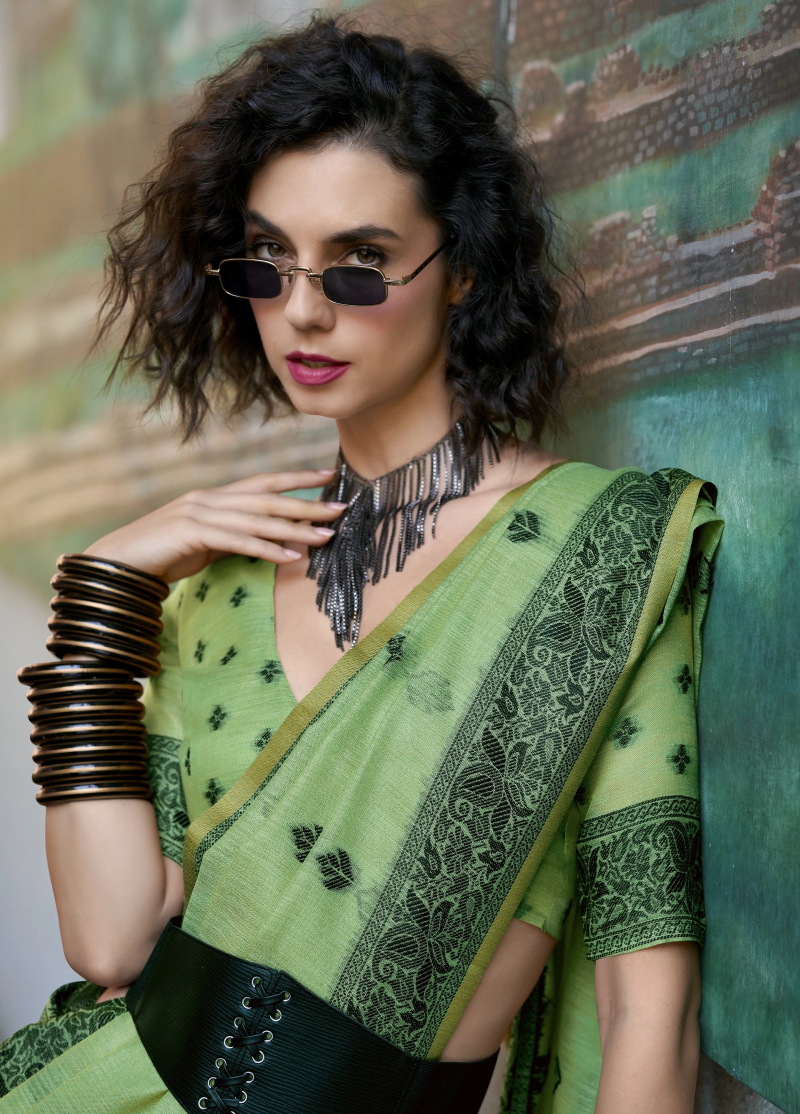 Woman wearing a green saree with a textured wall background