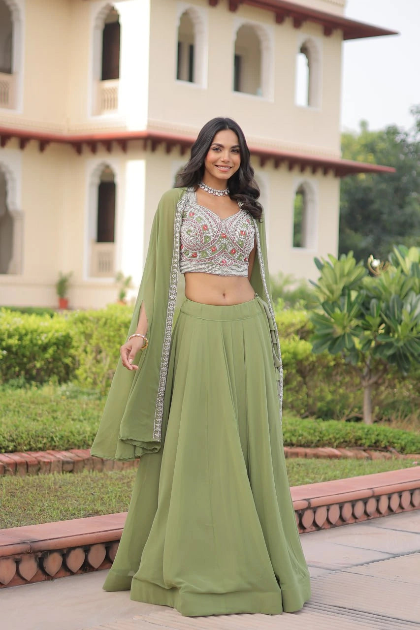 Woman in a green traditional outfit standing outdoors with a building and greenery in the background