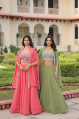 Two women in traditional pink and green outfits standing in front of a building with a garden.