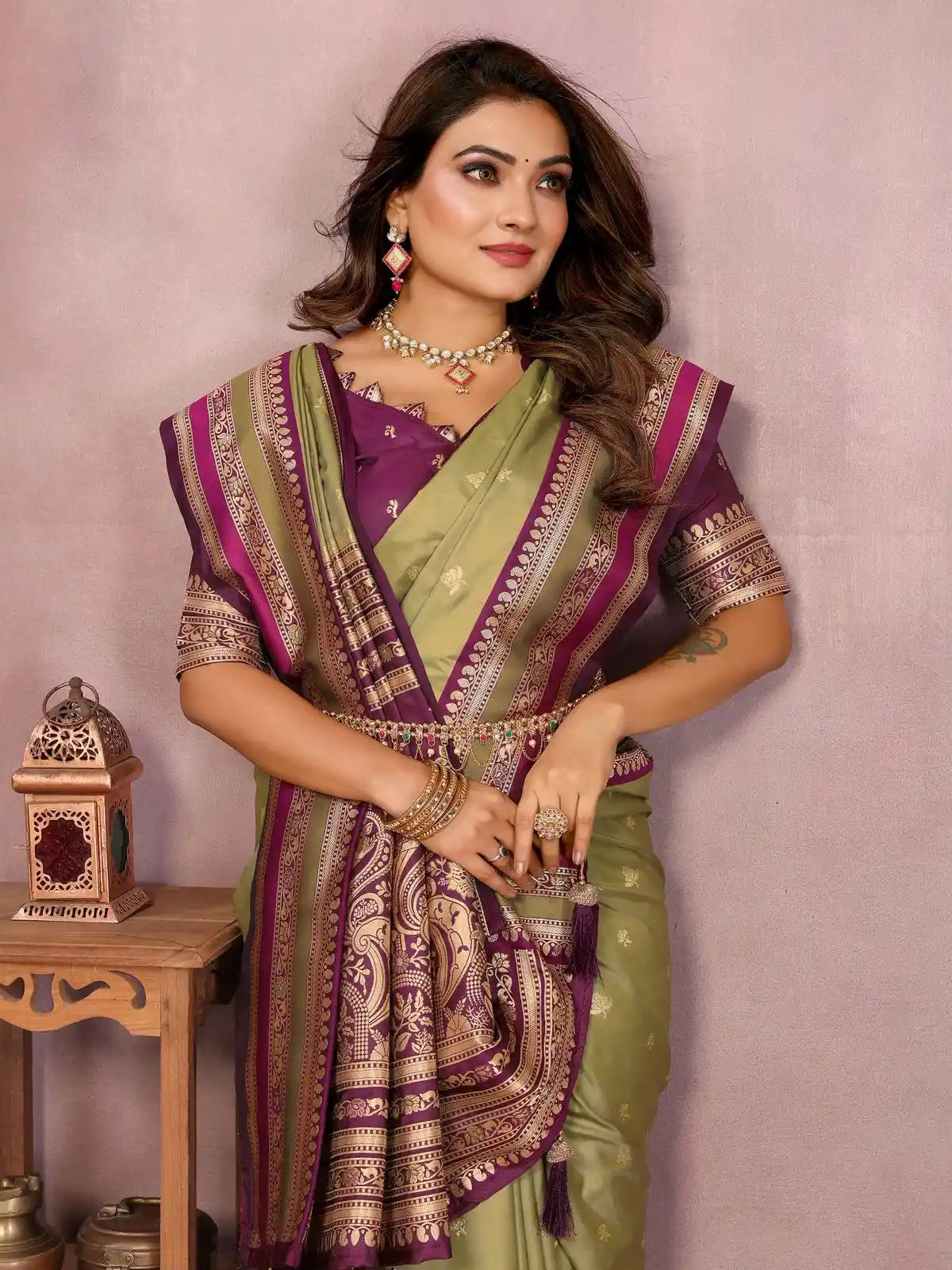 Woman wearing a traditional saree with a purple and green pattern against a light pink background