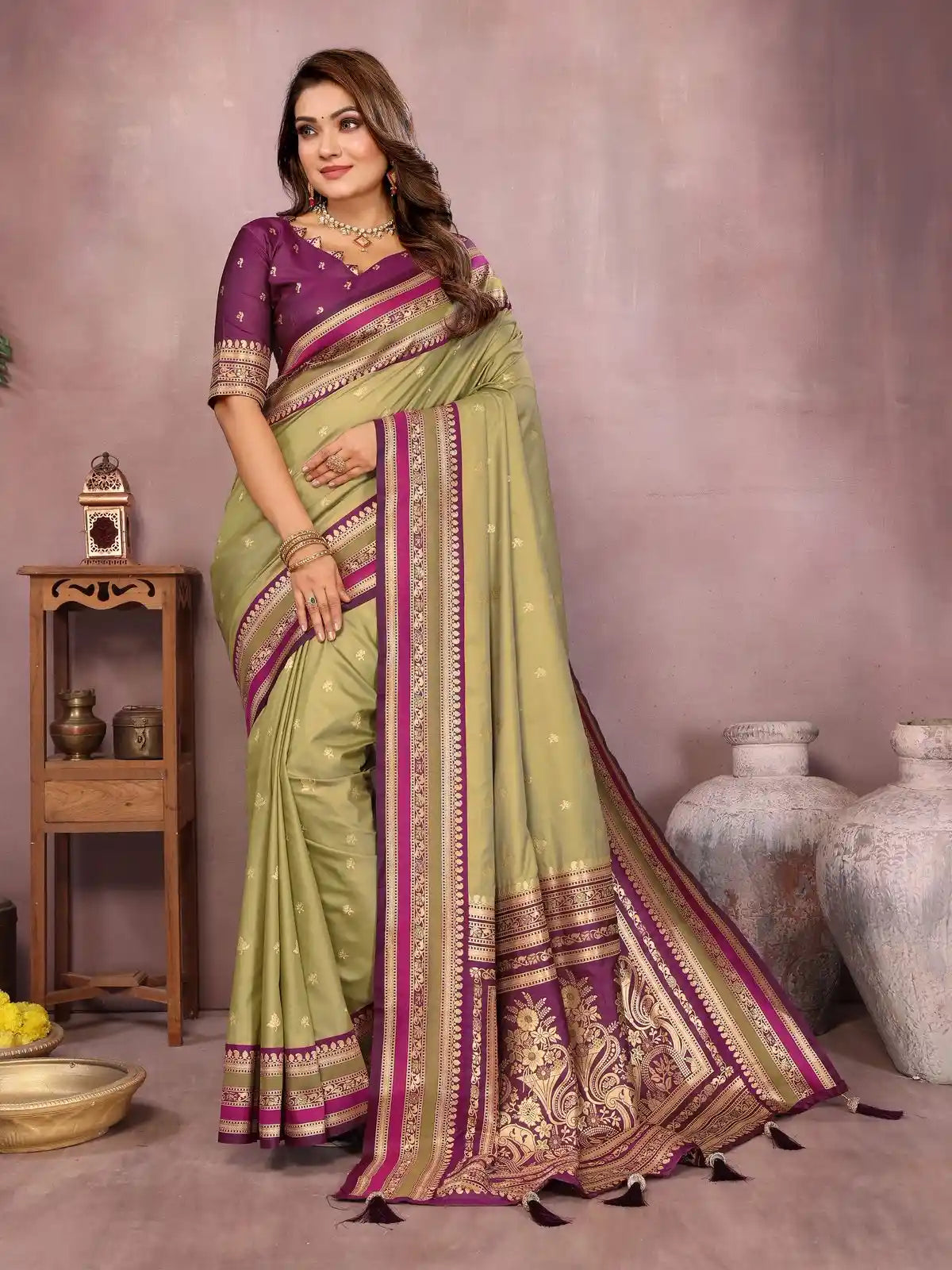 Woman wearing a green and purple saree with a decorative border in a room setting.