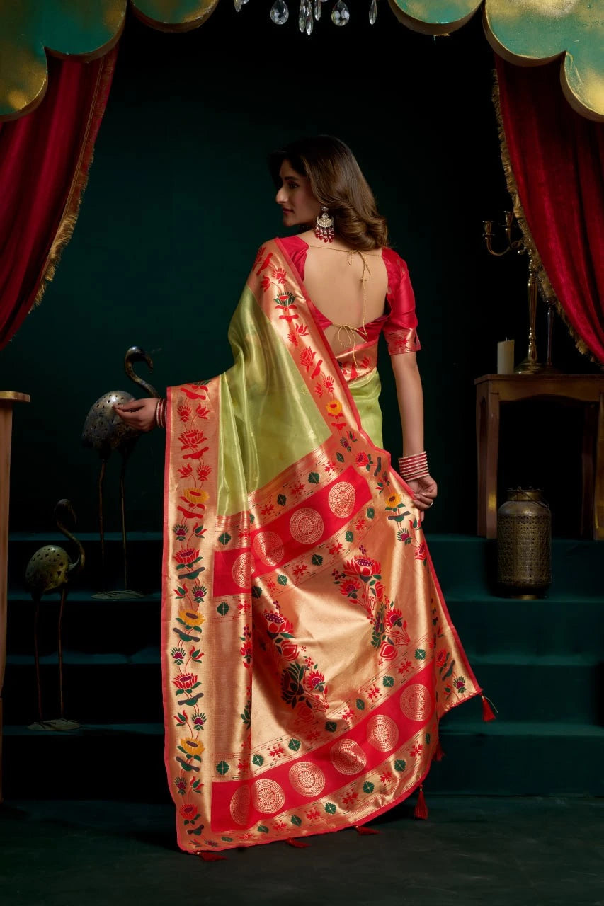 Woman in a colorful saree standing on a stage with red curtains and stage lights.
