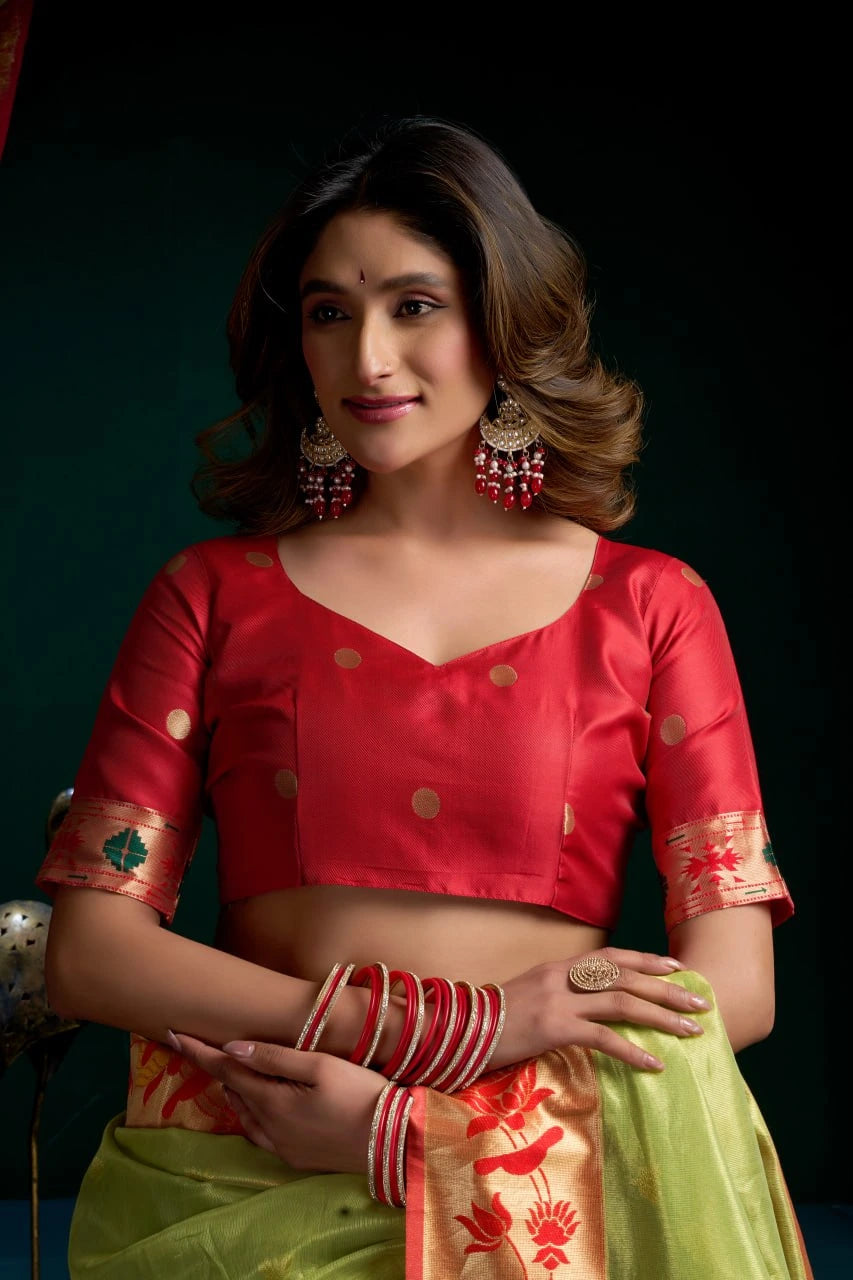 Woman wearing a red blouse with gold patterns and a green saree with red patterns against a dark background