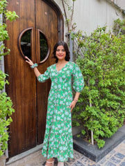 Woman in a green floral dress standing next to a wooden door with circular design.