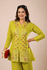 Woman wearing a green embroidered outfit with a red clutch against a beige background