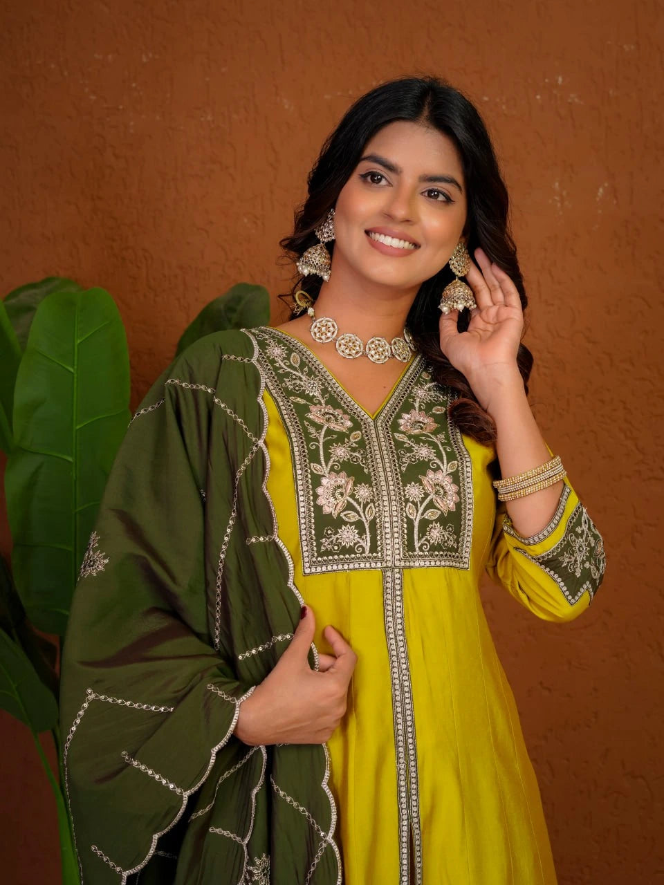 Woman wearing a green and yellow traditional outfit with jewelry against a brown background