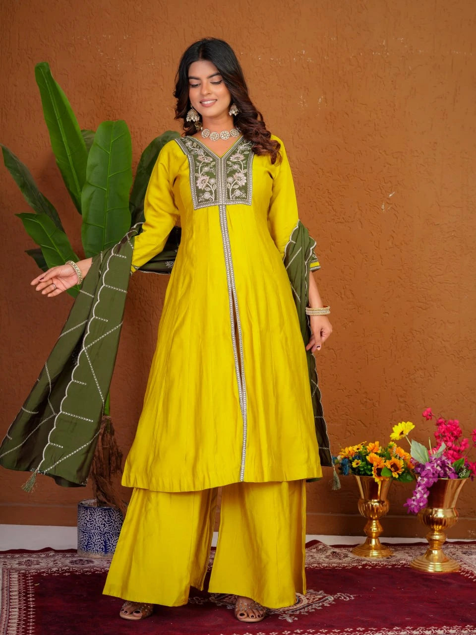 Woman in a yellow traditional outfit with green dupatta against a brown wall.