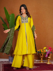 Woman in a yellow traditional outfit with green dupatta against a brown wall.