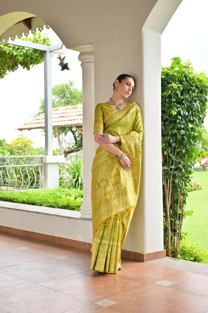 Woman in a green saree standing on a porch with greenery in the background