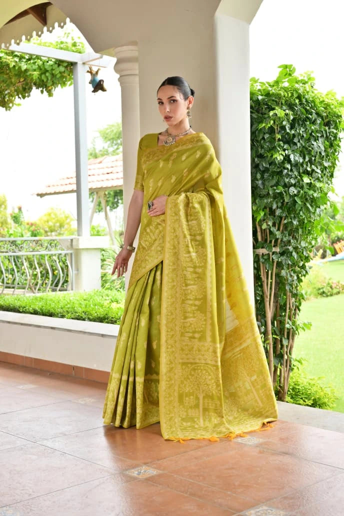 Woman in a yellow saree standing on a porch with greenery in the background