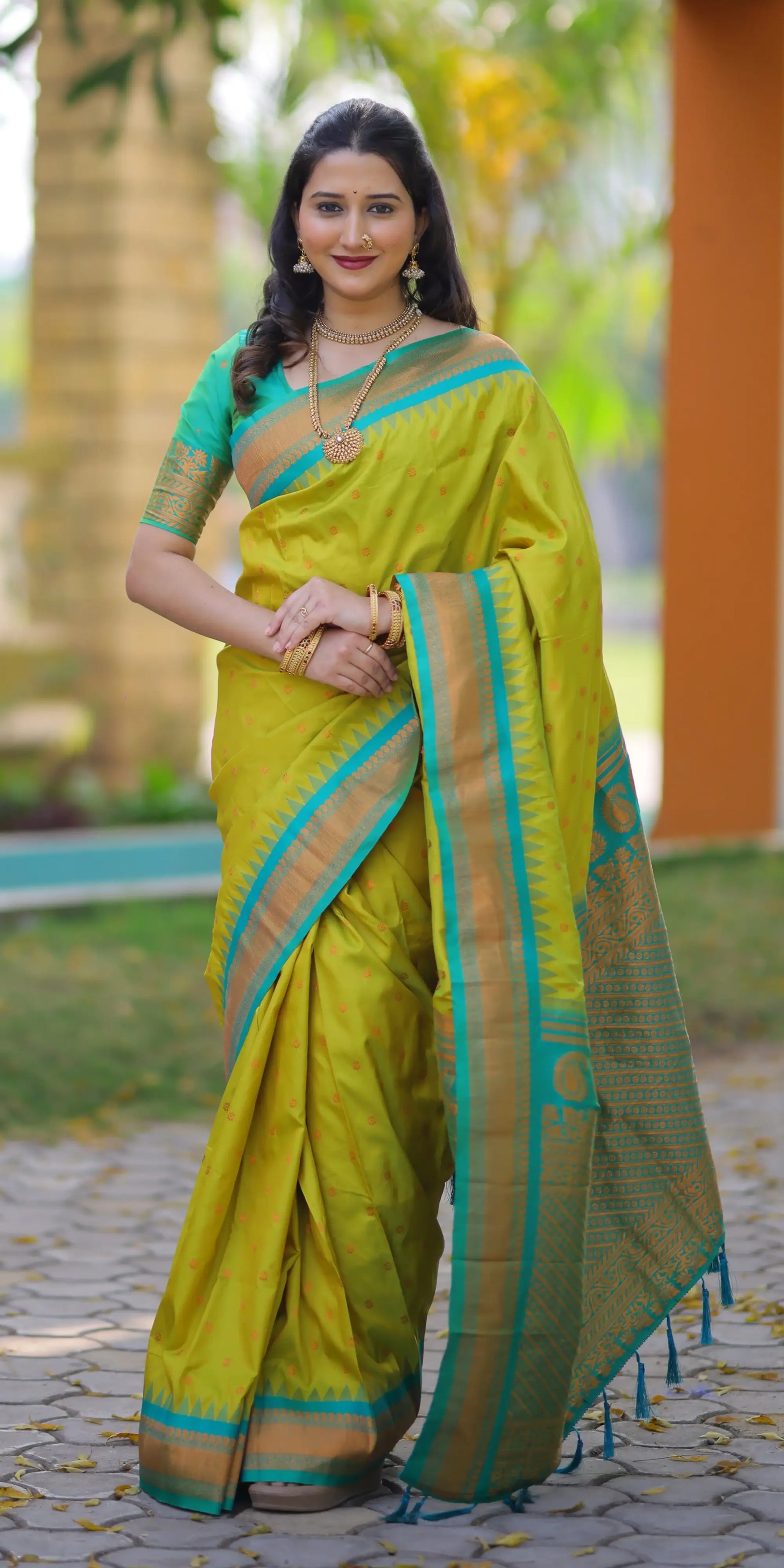 Woman wearing a green saree with a blue border outdoors.