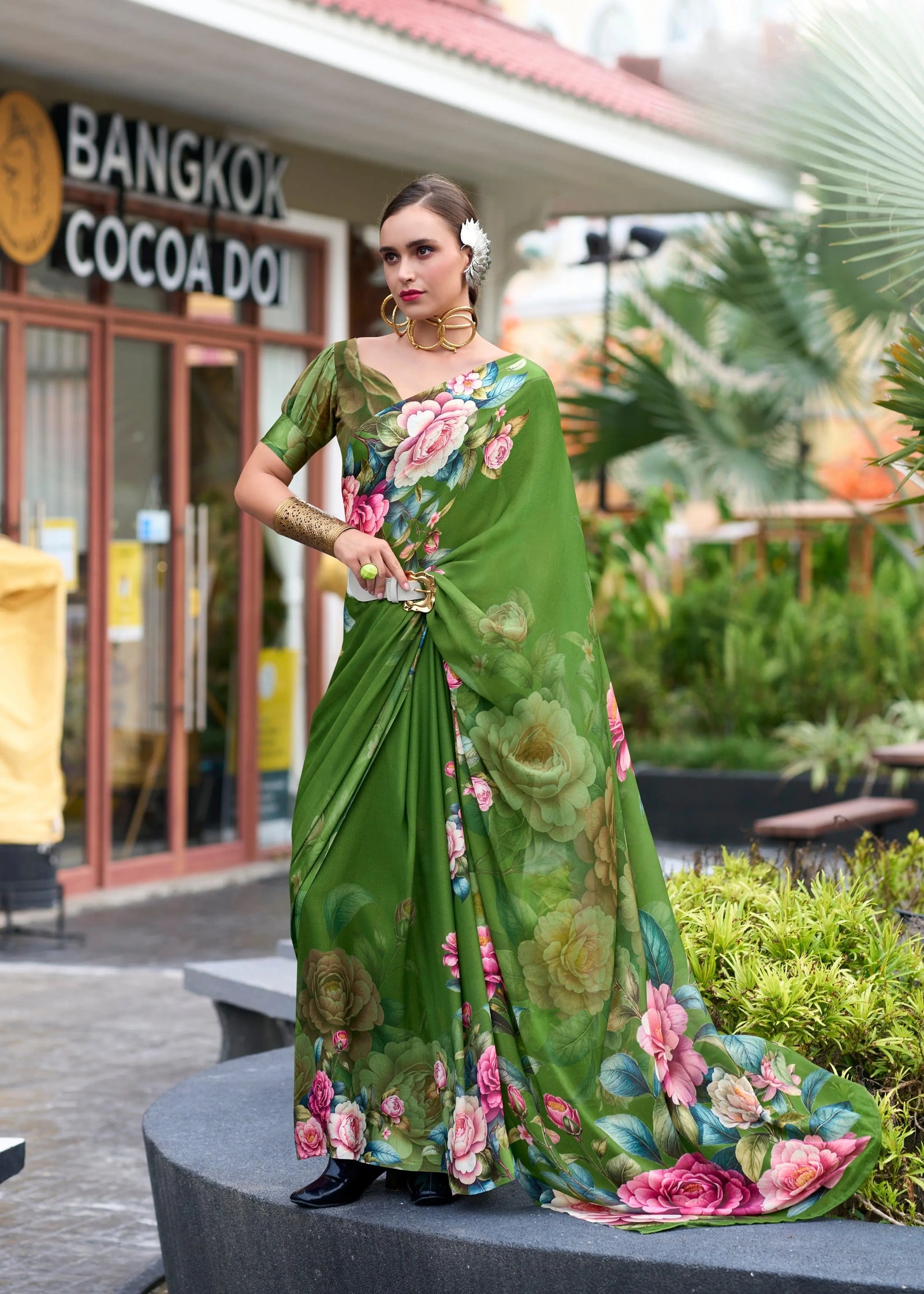 Woman in a green floral saree standing outdoors with 'Bangkok Cocoa Door' in the background