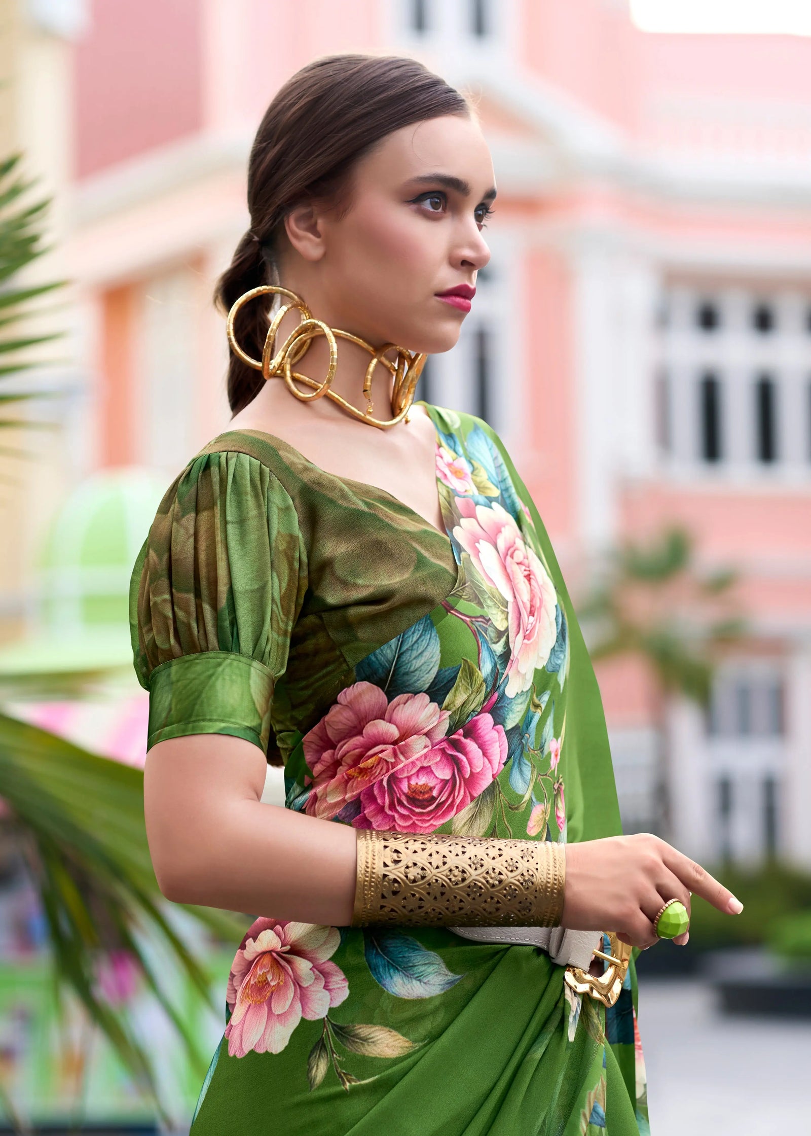 Woman wearing a green floral saree with gold jewelry in an outdoor setting