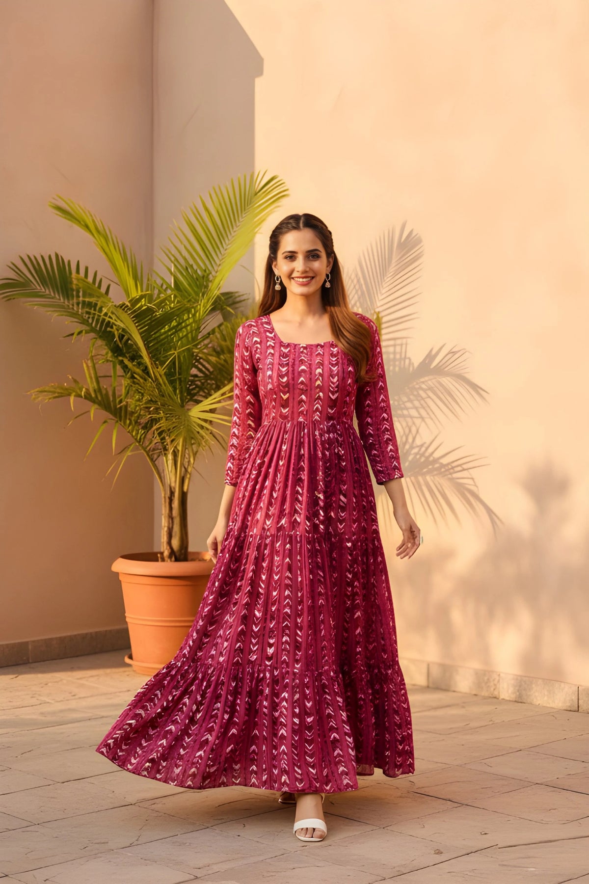 A front-facing full-length shot of a woman smiling and walking forward in a long, tiered magenta dress with white geometric patterns.