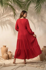 Woman in a red dress standing in a warm, outdoor setting with plants and vases.
