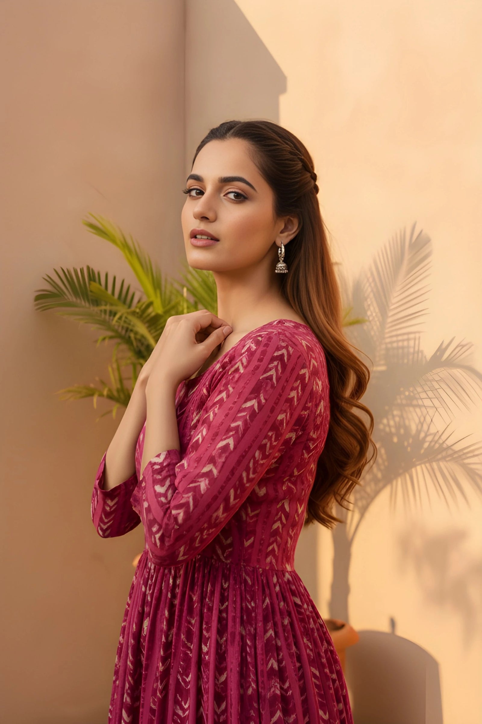 A side profile medium shot of a woman in a magenta printed dress, looking toward the camera with a palm plant in the background.