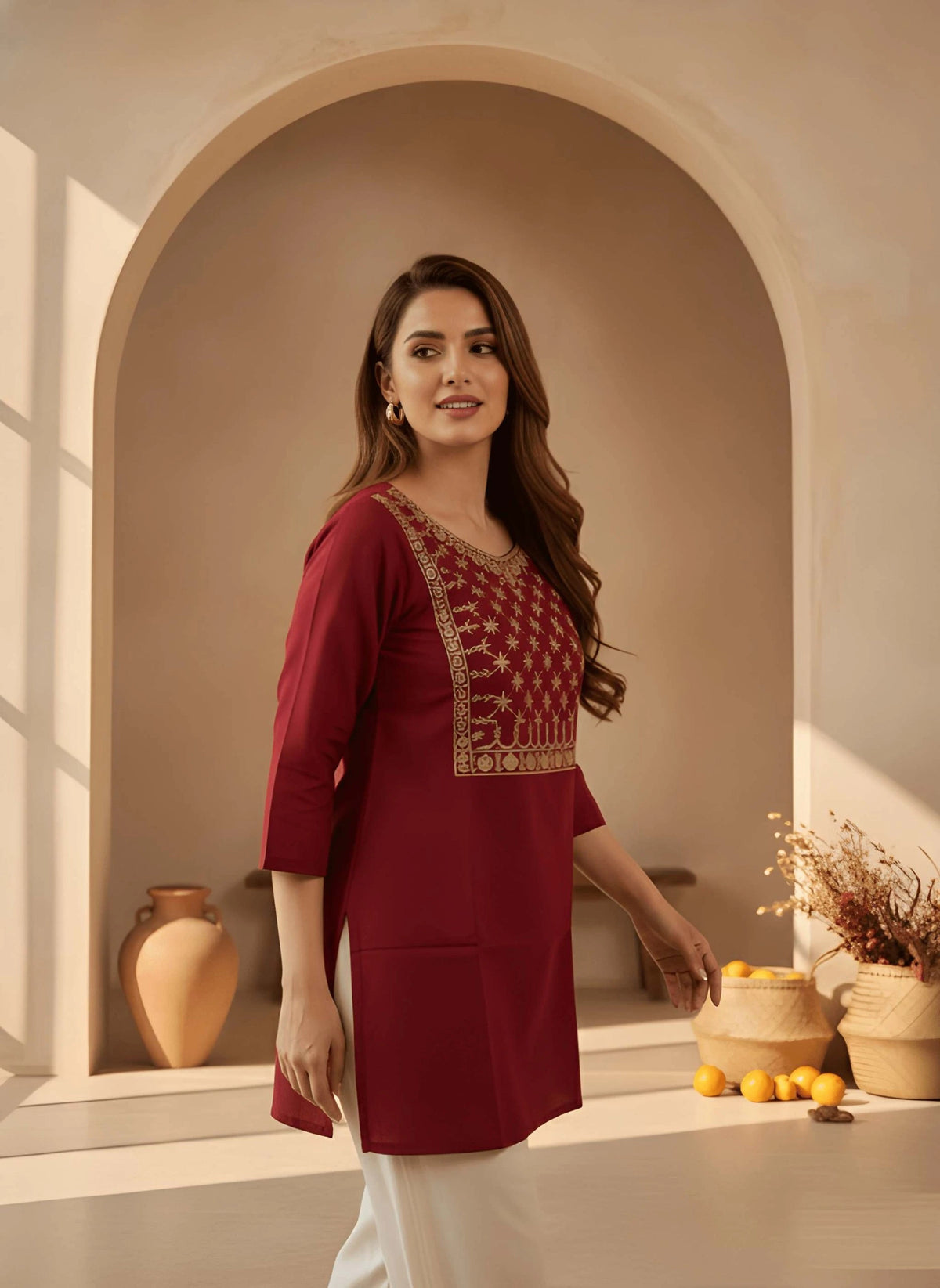 Woman in a red traditional outfit standing in a decorative room with arches and vases.
