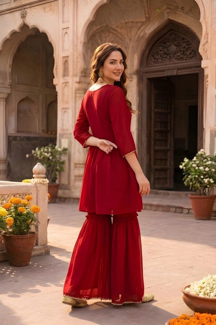 Woman in a red outfit standing in an outdoor setting with arches and plants.