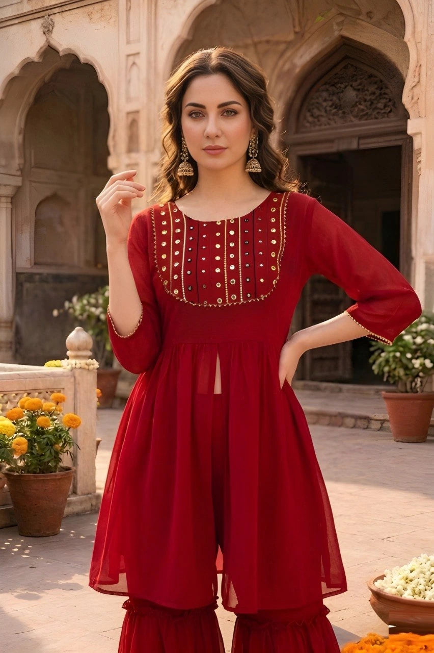 Woman in a red traditional outfit standing in an outdoor setting with architectural elements.