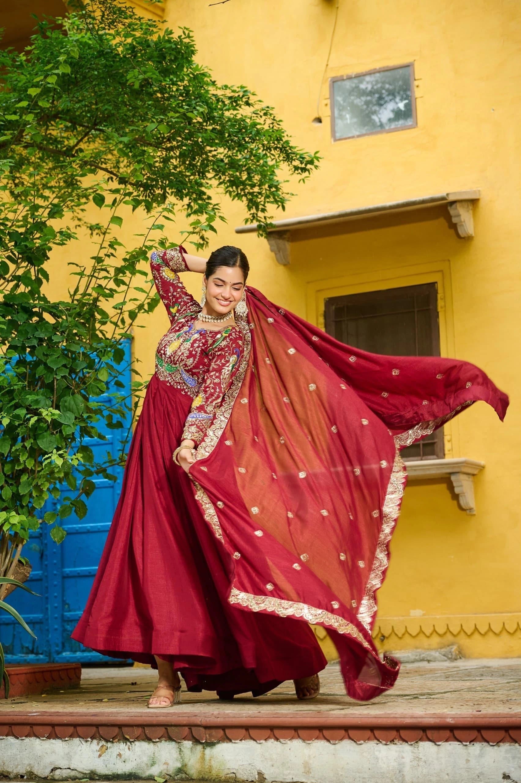 Woman in a red traditional outfit standing in front of a yellow wall with a blue baseboard.
