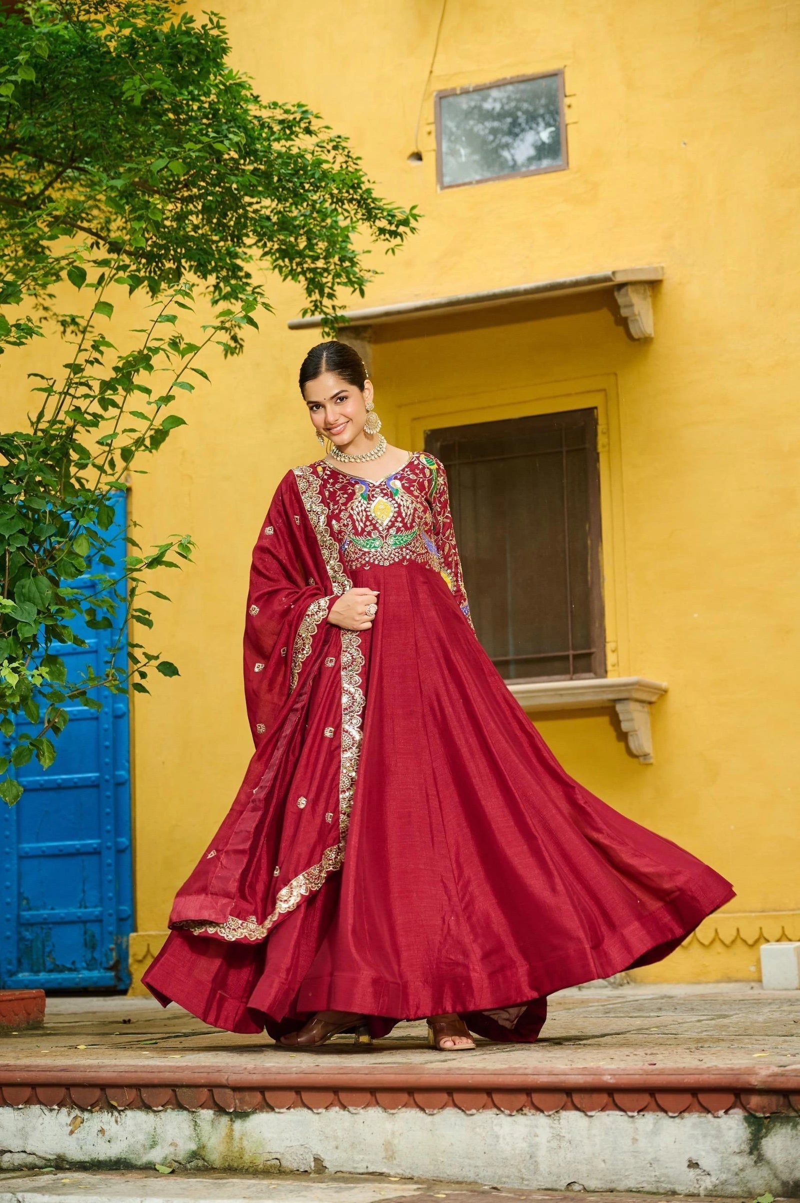 Woman in a red traditional outfit standing in front of a yellow wall with a blue door.