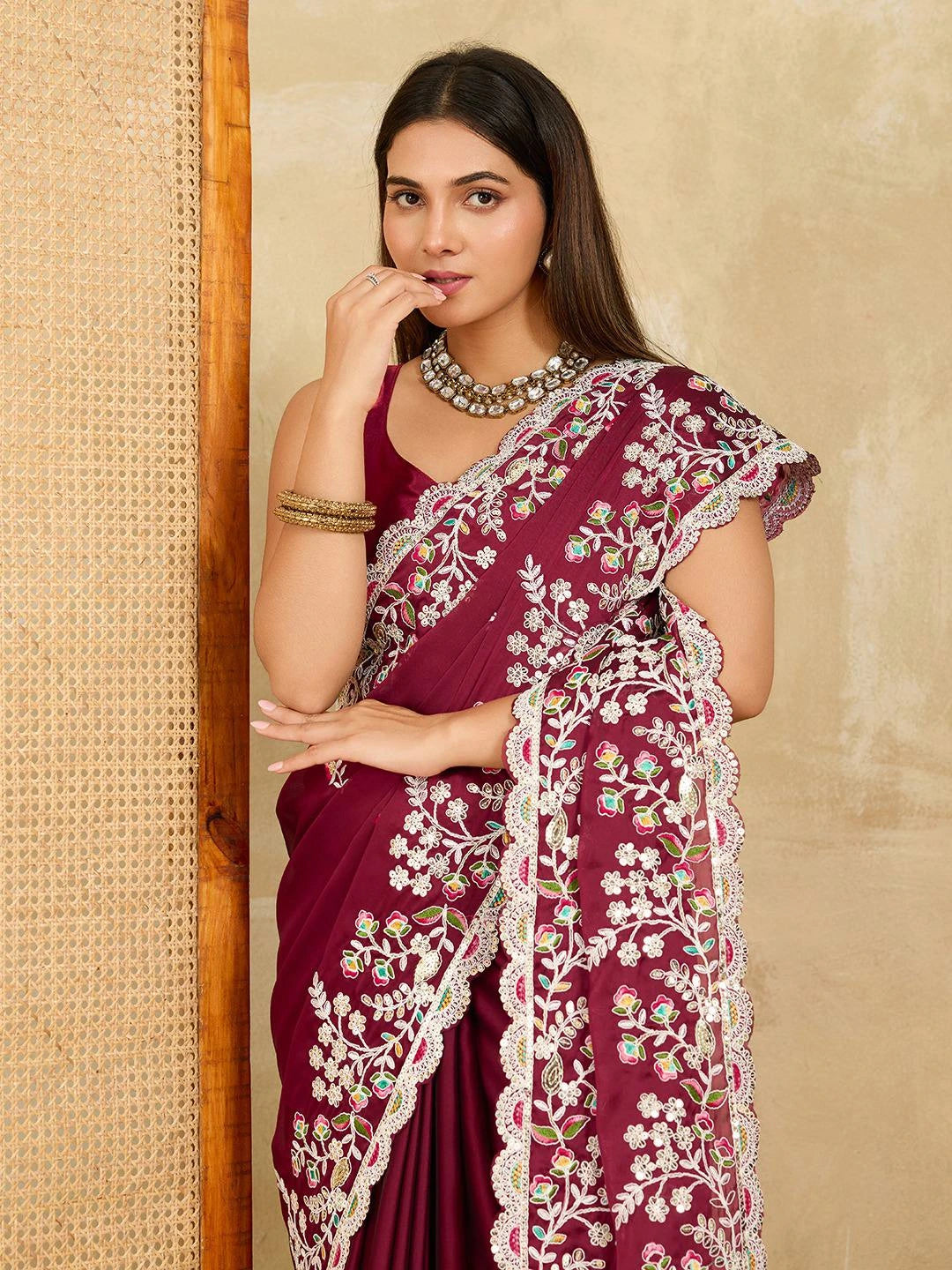 Woman wearing a maroon saree with white embroidery against a beige wall.