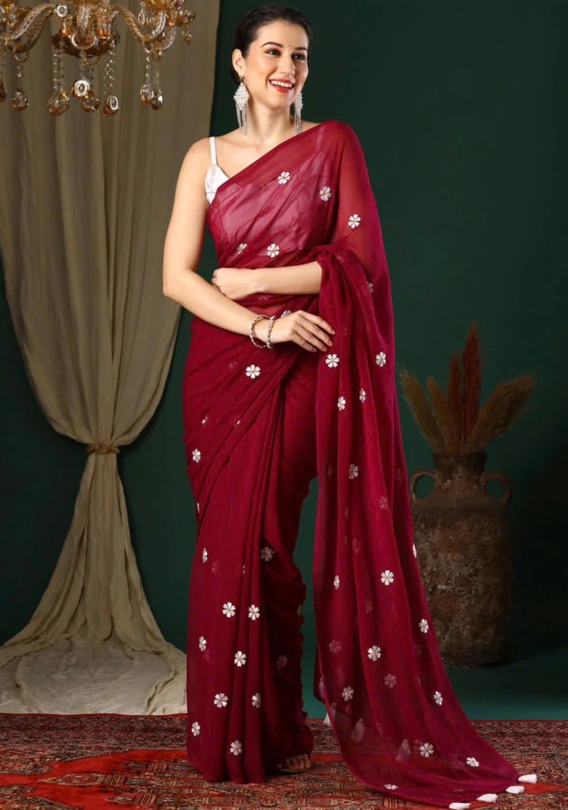 Woman wearing a red saree with white patterns against a dark green background