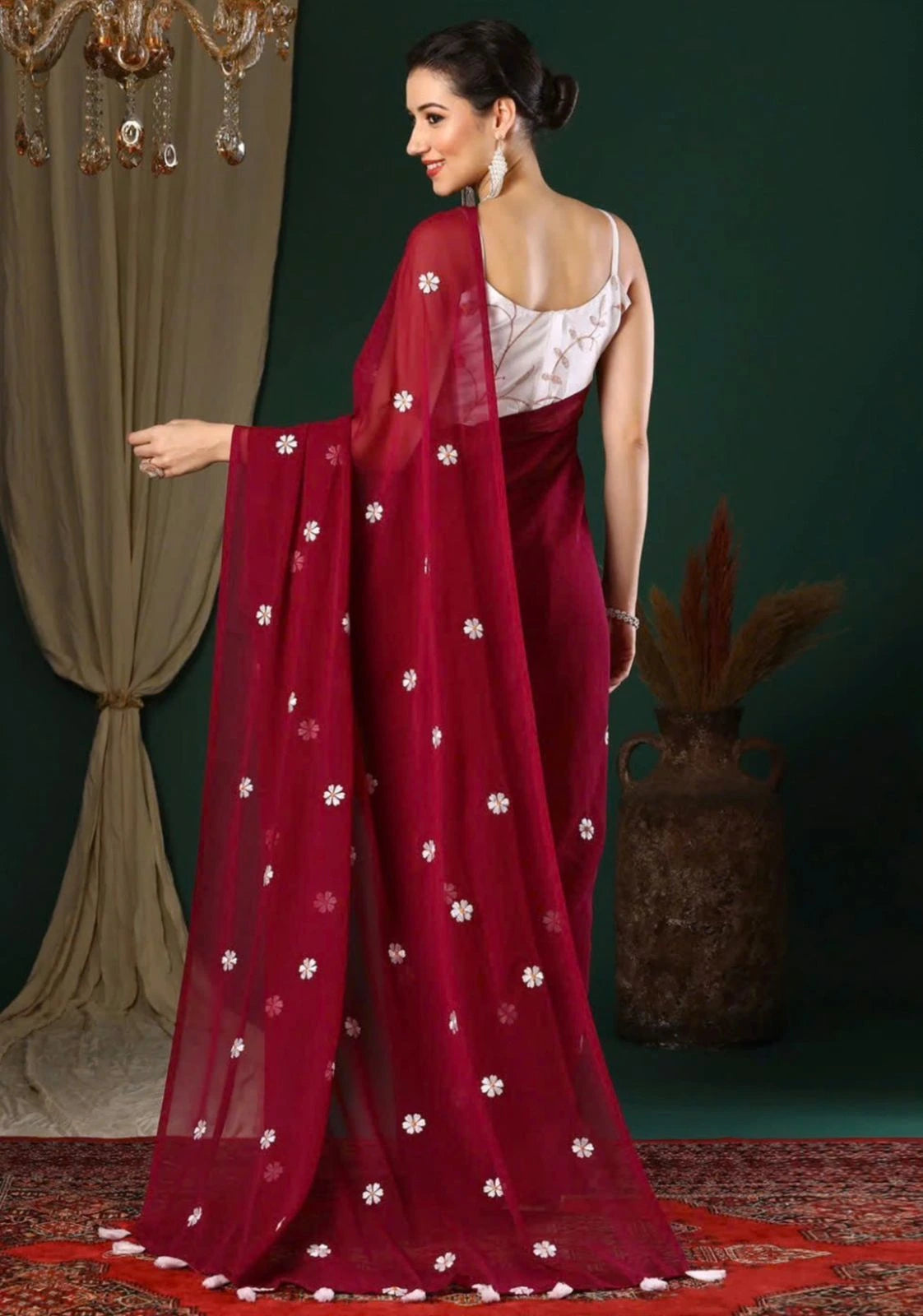 Woman wearing a red saree with white floral patterns in a decorated room.