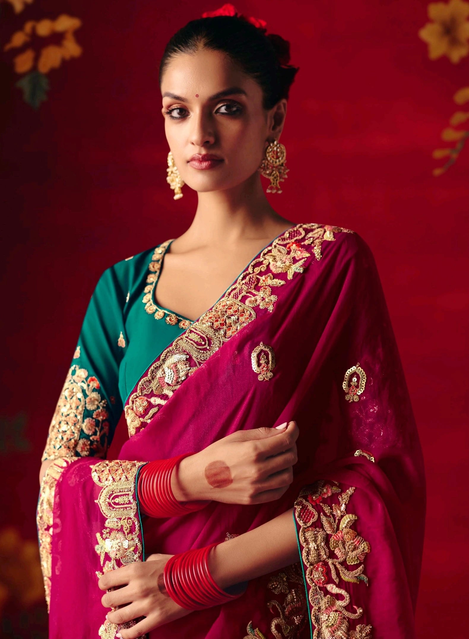 Woman wearing a traditional saree with intricate designs against a red background