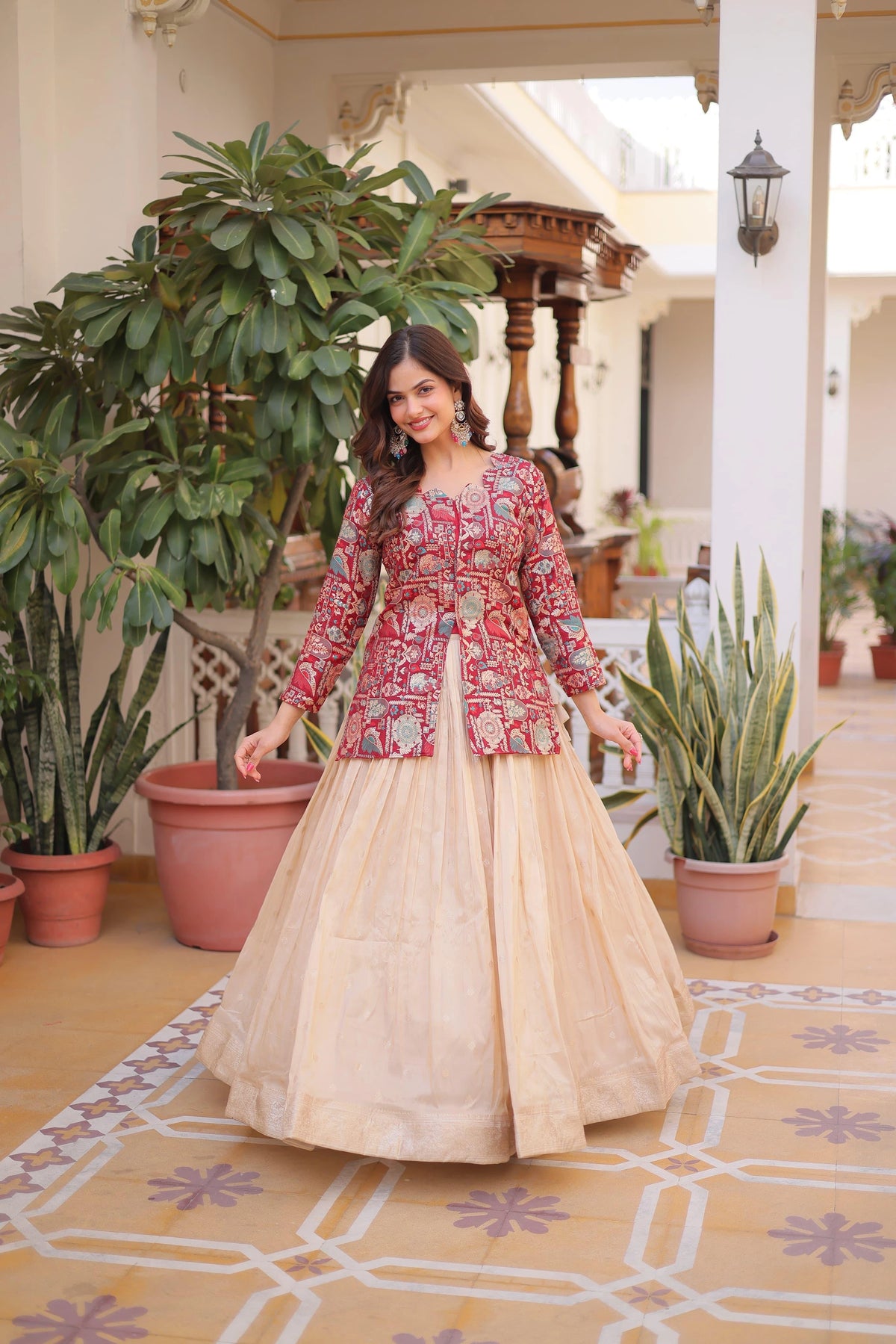 Woman in a red and beige traditional outfit standing in a decorated indoor setting with plants.
