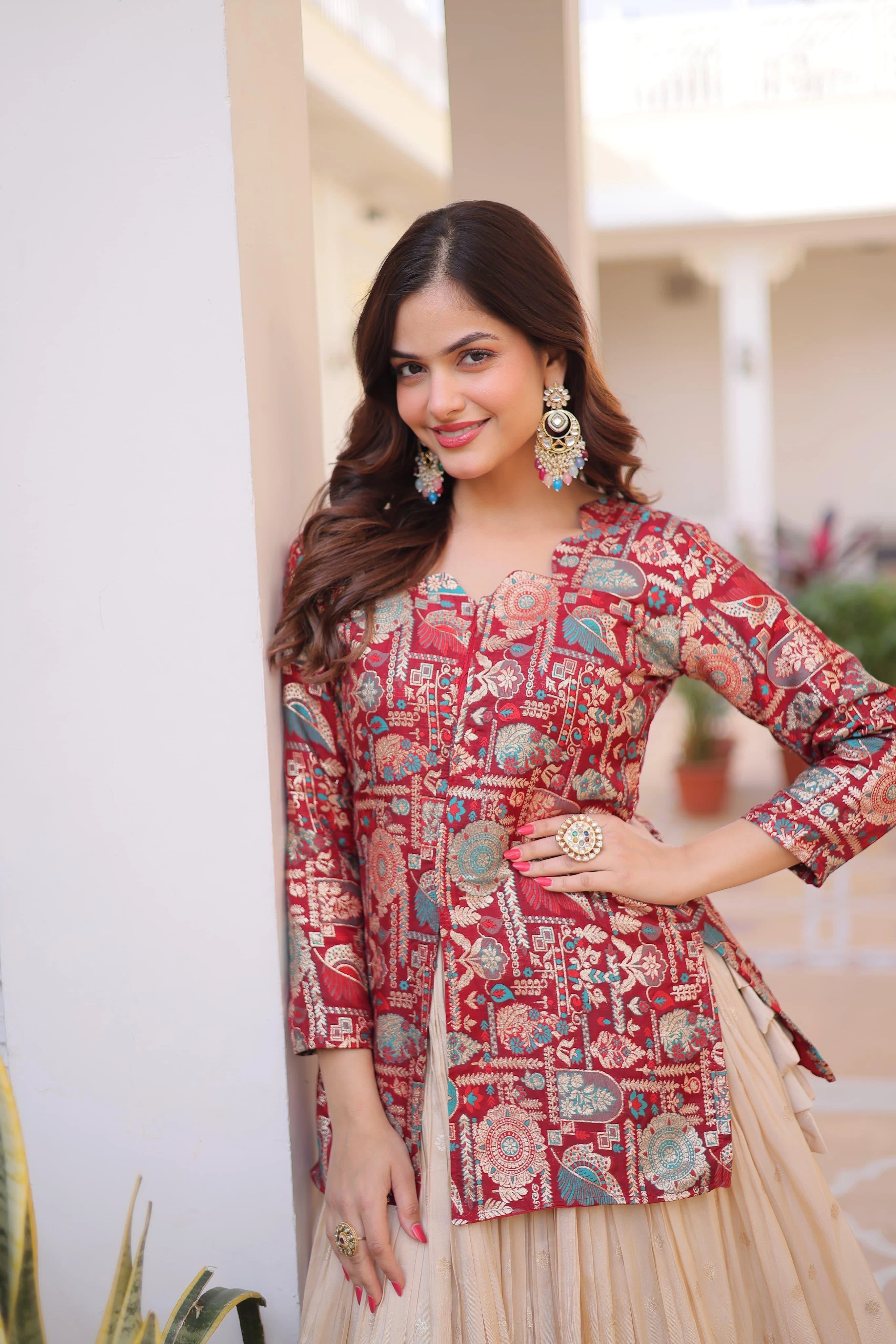 Woman wearing a patterned red and beige traditional outfit with jewelry, standing outdoors.