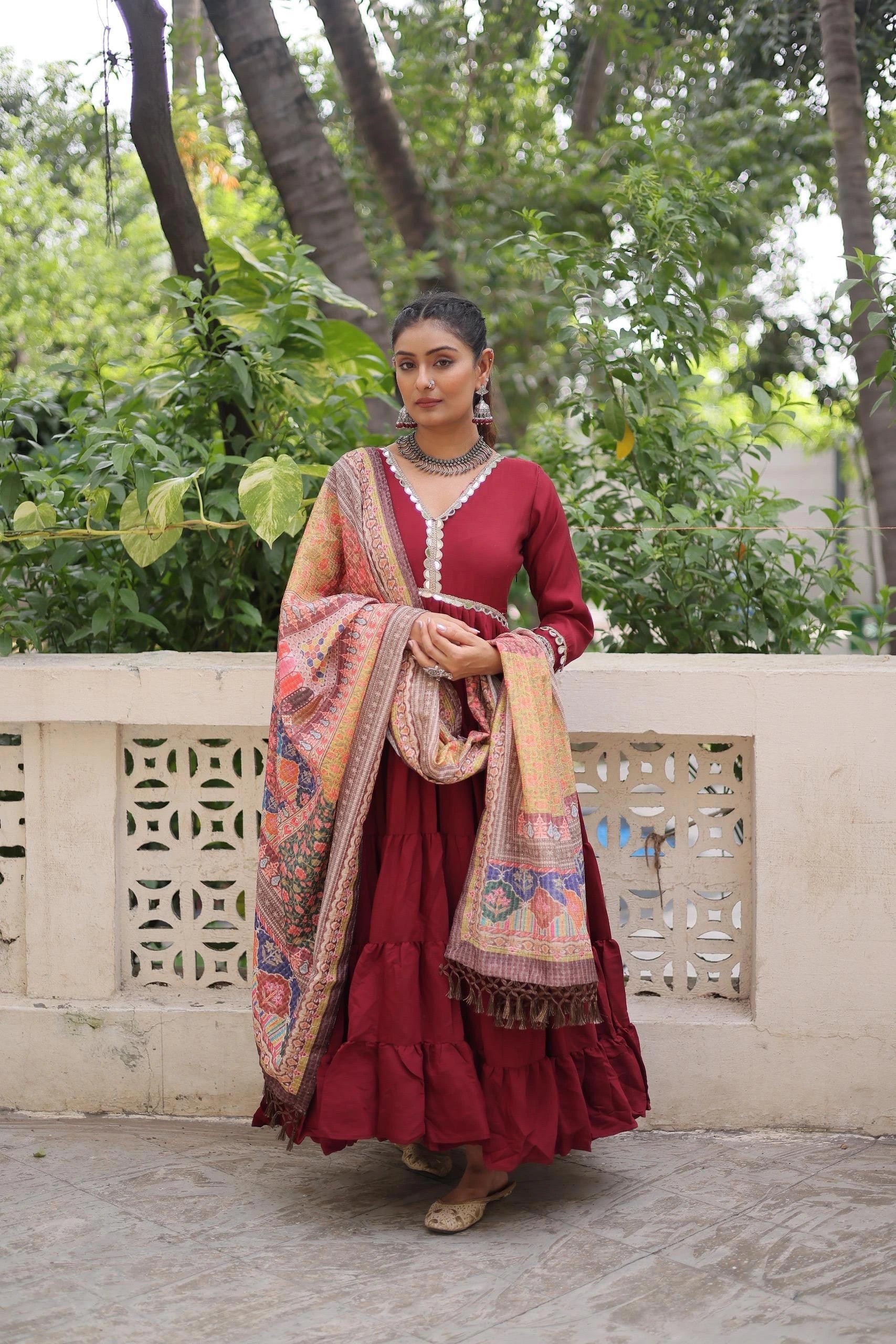 Woman in a red traditional outfit with a patterned shawl standing outdoors.