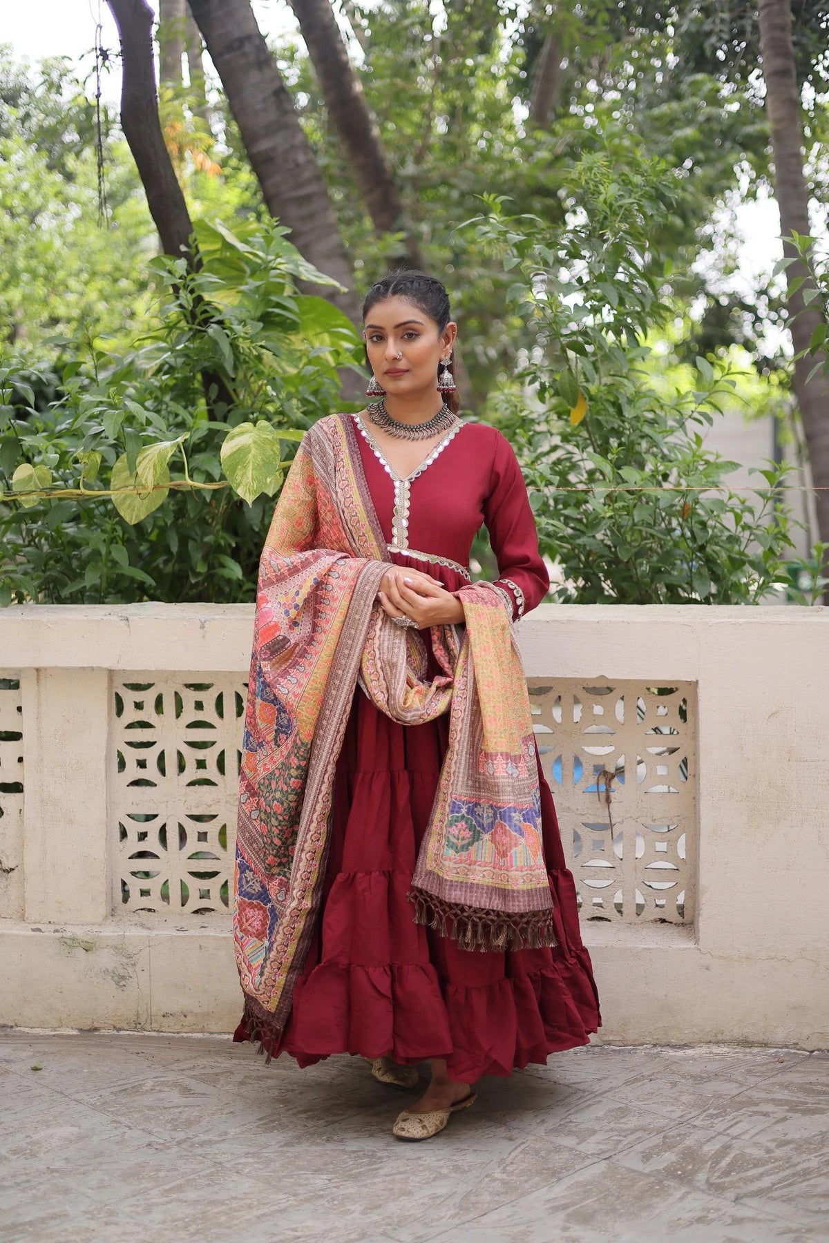 Woman in a red traditional outfit with a patterned shawl standing outdoors.