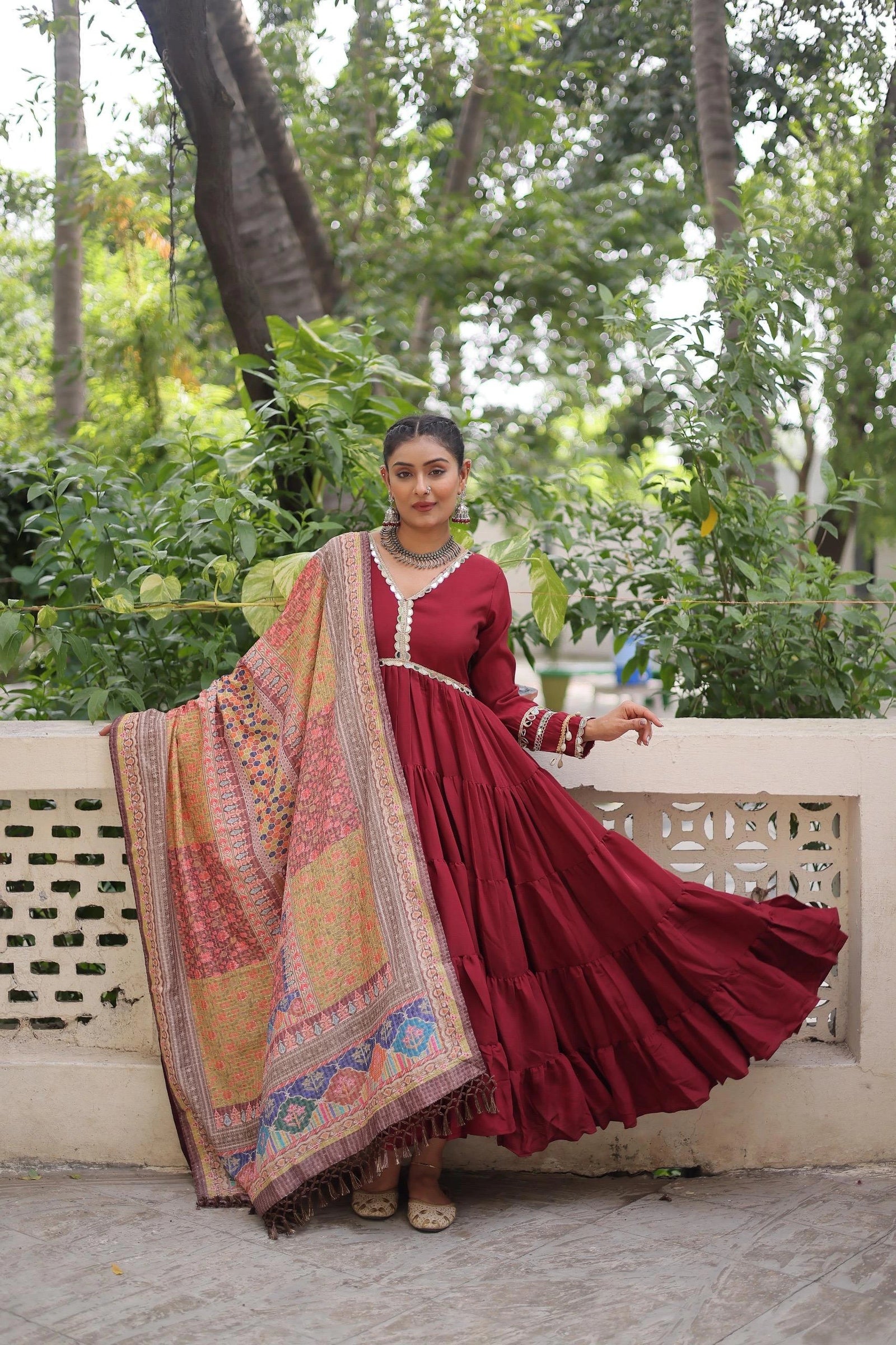 Woman in a red traditional outfit with a patterned dupatta standing outdoors.