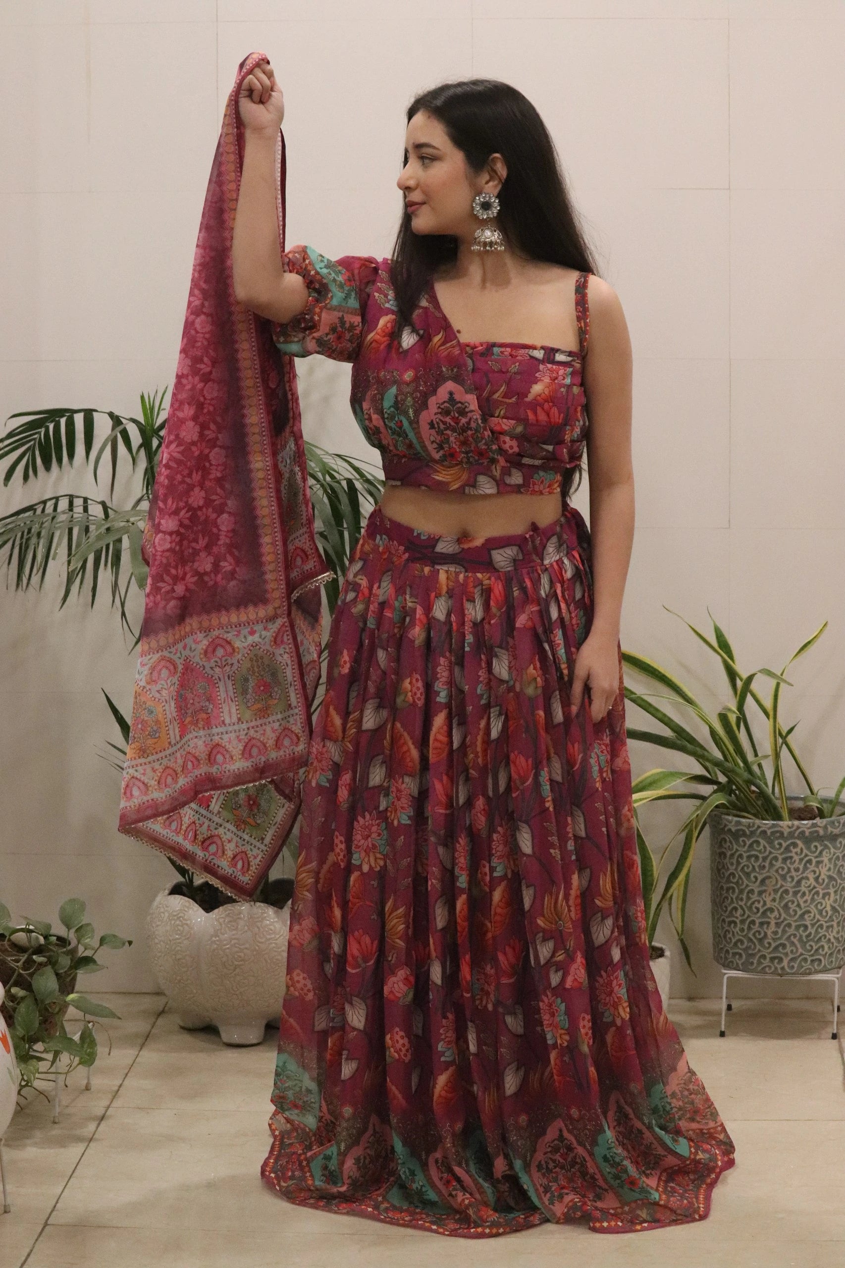 Woman in a floral outfit holding a matching dupatta with plants in the background
