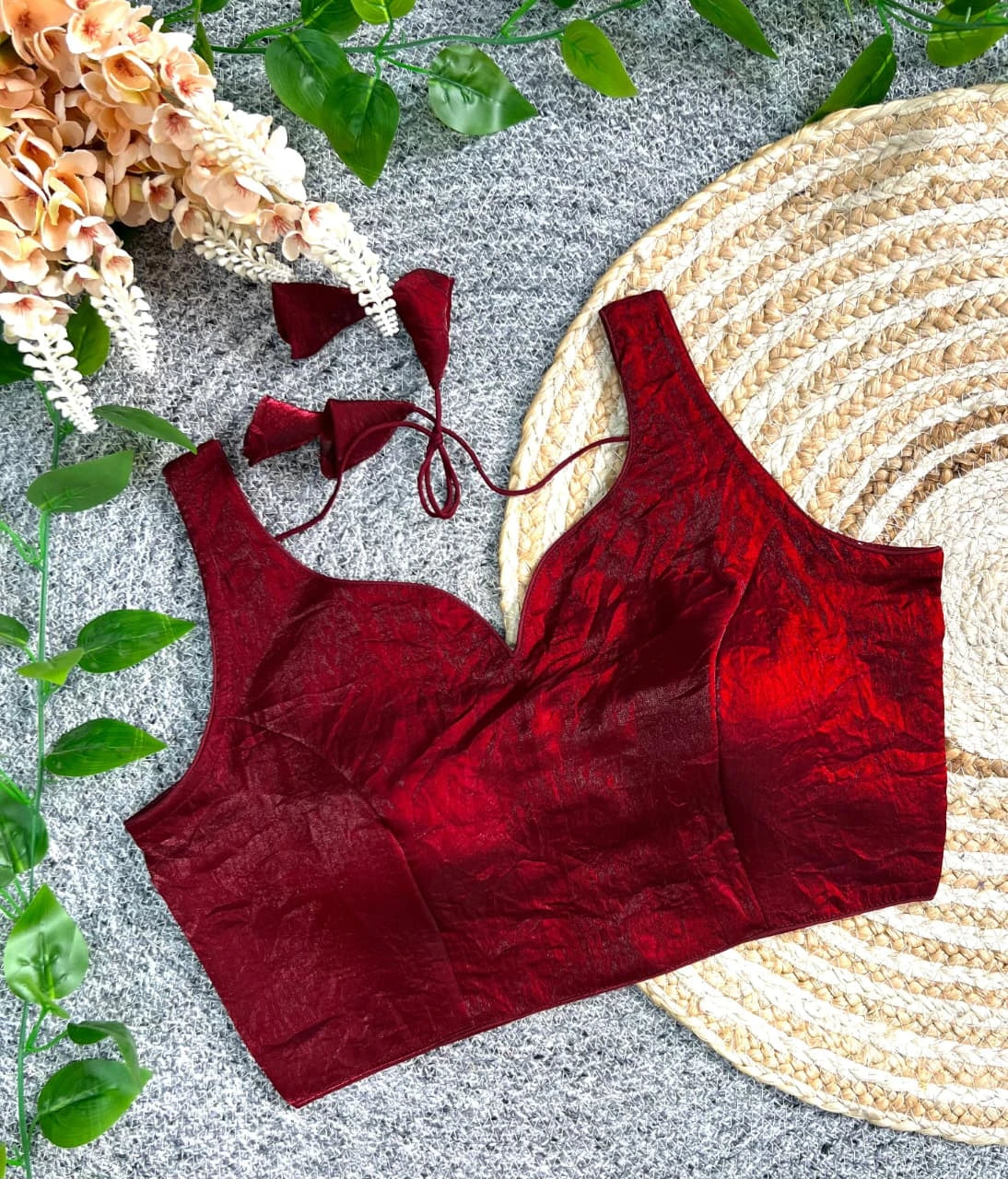 Red velvet top with matching earrings on a textured surface with leaves and flowers.