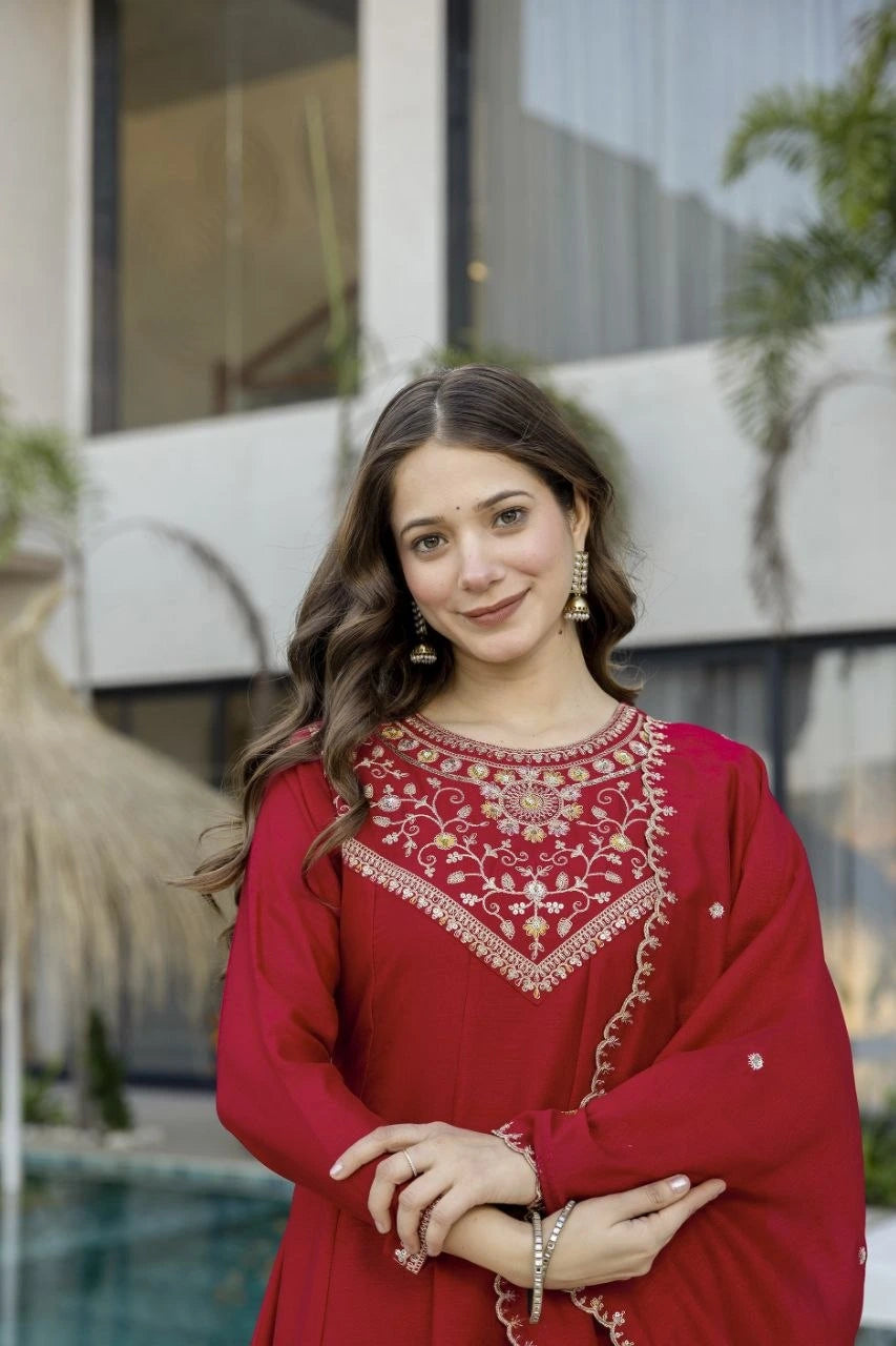 Woman wearing a red traditional outfit with intricate patterns, standing outdoors.