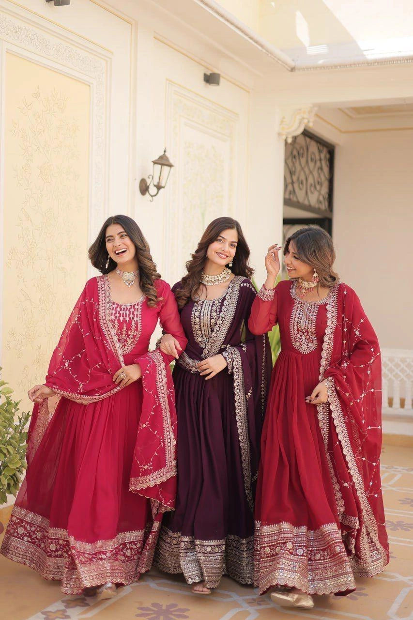 Three women in traditional red and purple dresses with intricate designs indoors.