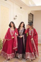 Three women in traditional red and purple dresses with intricate designs indoors.