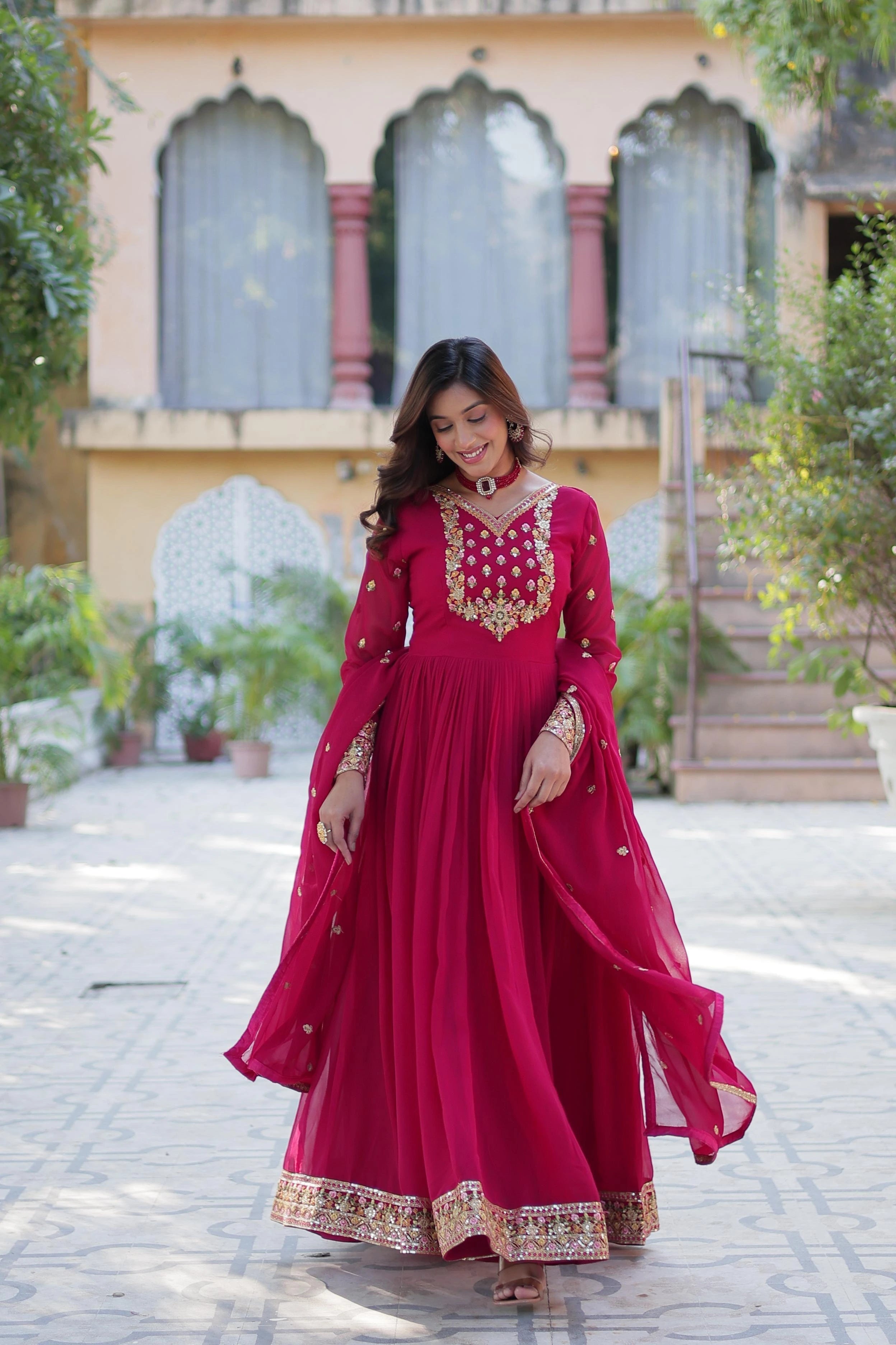 Woman in a red traditional outfit with gold embroidery standing outdoors.